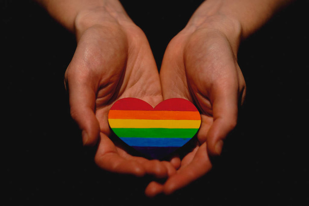 Female arms holding the heart coloured in LGBT pride colours on the dark background. Concept of the International Day Against Homophobia concept, sexual equality, feminism, social safety and protectio - Photo, Image