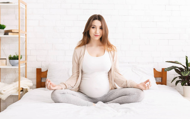 Calm young pregnant woman meditating in bed - Photo, Image