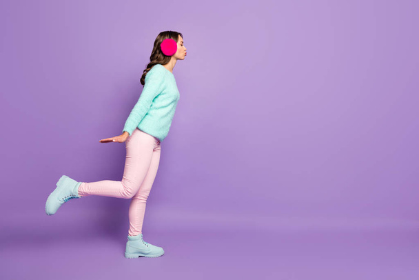 Full body profile photo of pretty curly lady send air kiss empty space blind date experience wear fuzzy pullover pink pastel warm ear covers pants boots isolated purple color background - Photo, Image