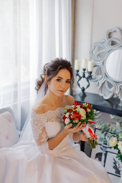 Όμορφη ευτυχισμένη νύφη σε ένα δωμάτιο με ένα γαμήλιο μπουκέτο. - Φωτογραφία, εικόνα