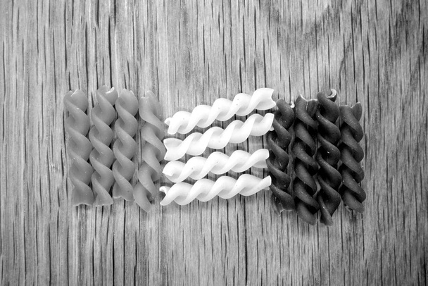 Droge meerkleurige pasta op houten plank in zwart-wit. - Foto, afbeelding