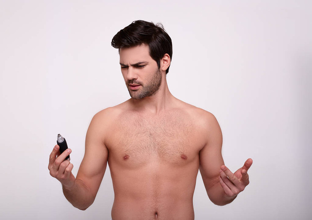 A charming muscular man holds a trimmer in his hand to remove unwanted hair. - 写真・画像