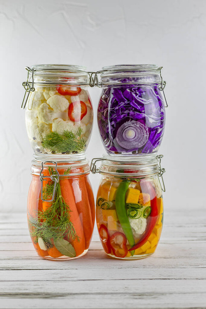 Glasgläser mit fermentiertem Rotkohl, Blumenkohl, Gurken, Zwiebeln, Möhren, Gemüse auf hellem Hintergrund. Fermentation ist eine Quelle probiotischer - Foto, Bild