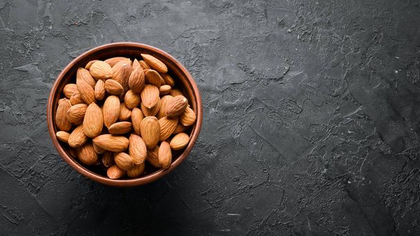 Almond nut in a bowl. Nuts on a black stone background. Top view. Free space for your text. - Zdjęcie, obraz
