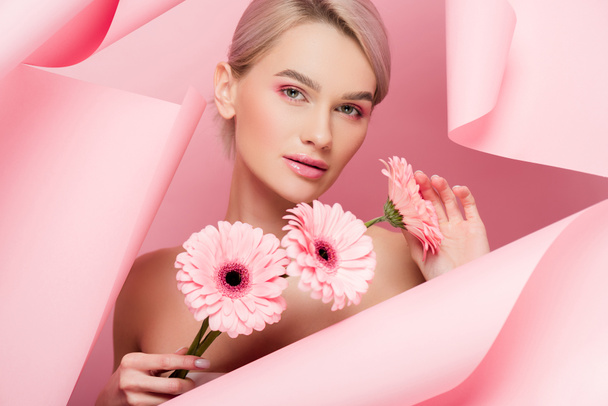 attractive girl with pink flowers and makeup in torn paper, on pink - Фото, изображение