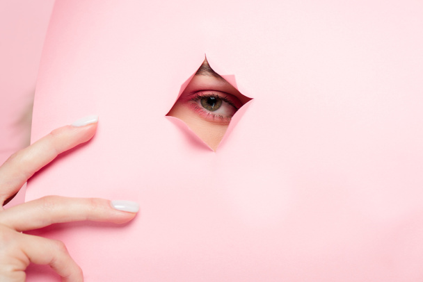 περικοπή άποψη του κοριτσιού με ροζ μακιγιάζ κοιτάζοντας μέσα από σχισμένο χαρτί  - Φωτογραφία, εικόνα