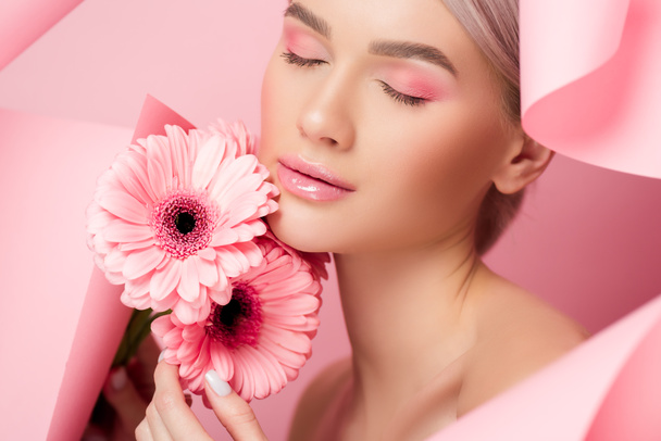tierna chica con los ojos cerrados sosteniendo flores de color rosa en papel roto, en rosa
 - Foto, imagen
