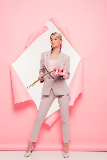 attractive stylish girl in suit holding flowers and posing in torn paper, on white - Foto, Imagen