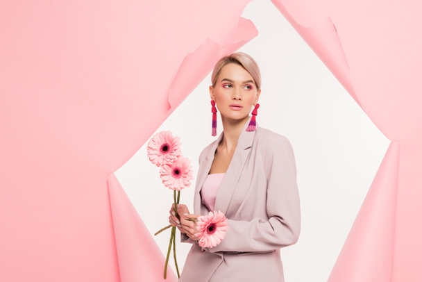 attractive blonde girl in stylish suit holding flowers and posing in torn paper, isolated on white - Fotoğraf, Görsel