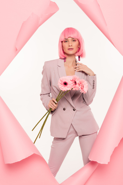 attractive stylish girl in suit and pink wig holding flowers and posing in torn paper,  isolated on white - Foto, Imagem