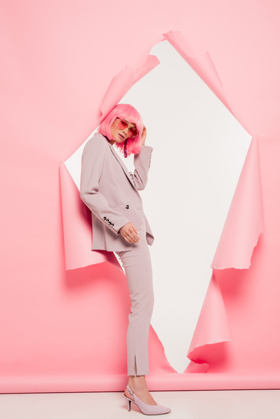 fashionable model in suit, sunglasses and pink wig posing in torn paper, on white - Foto, afbeelding
