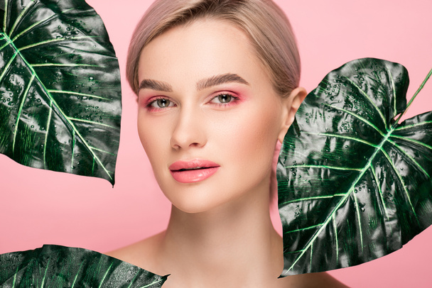 ελκυστική κοπέλα με ροζ μακιγιάζ που απομονώνονται σε ροζ με πράσινα φύλλα  - Φωτογραφία, εικόνα
