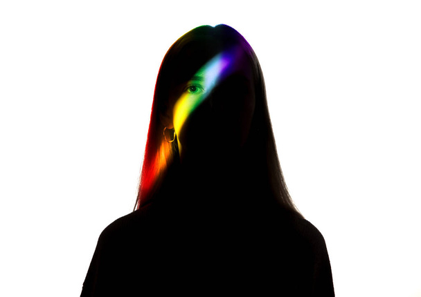 Dramatic portrait of a girl in the dark on white studio background with rainbow colored line - Zdjęcie, obraz