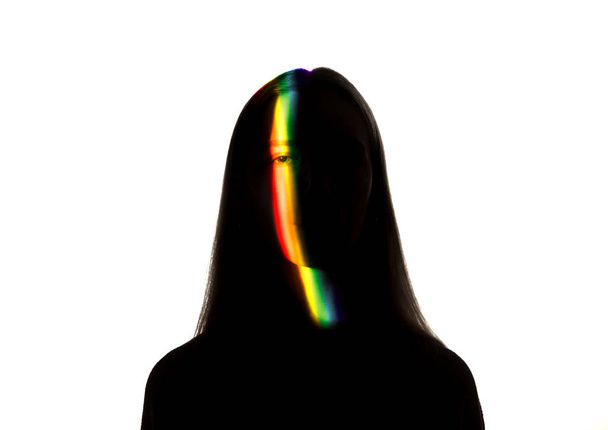 Dramatic portrait of a girl in the dark on white studio background with rainbow colored line - Zdjęcie, obraz