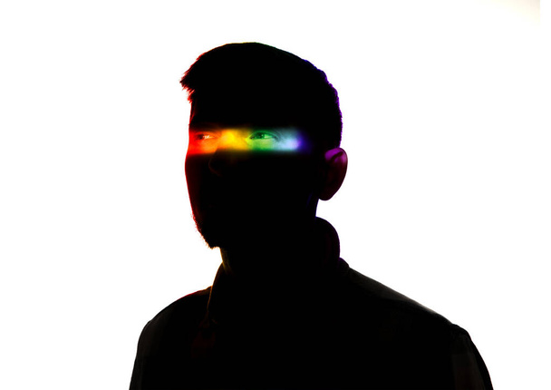 Dramatic portrait of a man in the dark on white studio background with rainbow colored line - Φωτογραφία, εικόνα