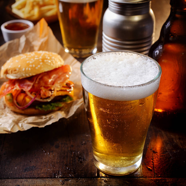 Glass of chilled beer served with a cheeseburger and French fries for a relaxing lunch in a pub or bar - 写真・画像