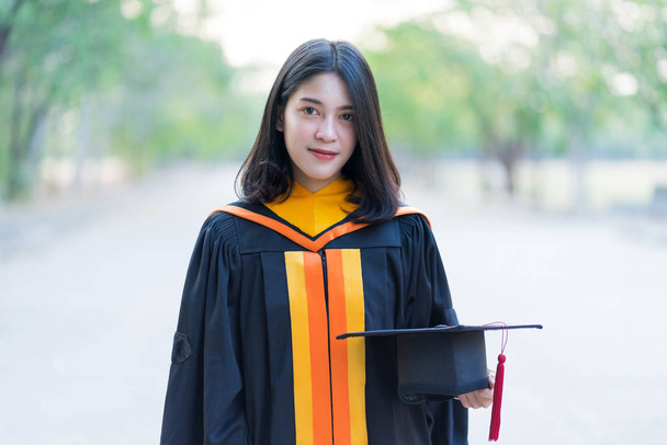 Retrato de una joven y alegre graduada vestida con una bata académica con gorra de graduado celebra su título universitario en el día de inicio en el campus universitario
. - Foto, imagen
