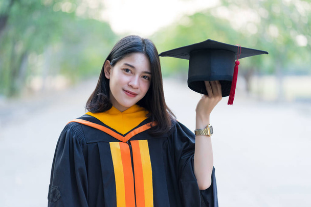 Portret młodej, wesołej absolwentki, noszącej akademicką suknię z czapką absolwentki świętuje swój dyplom uniwersytecki w dniu rozpoczęcia studiów na kampusie uniwersyteckim. - Zdjęcie, obraz