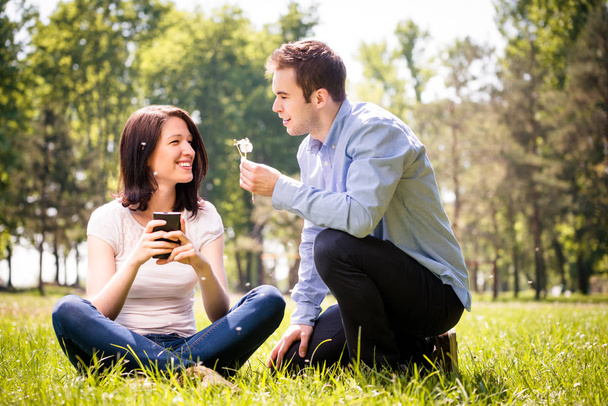 Young man blowing dandelion to face of his girlfriend holding mobile phone - Foto, Bild