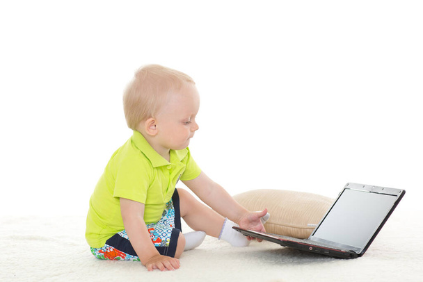 Bébé garçon de 1 an avec ordinateur portatif assis au sol sur un fond blanc. - Photo, image
