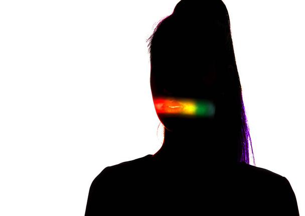 Δραματικό πορτρέτο ενός κοριτσιού στο σκοτάδι σε λευκό φόντο στούντιο με πολύχρωμη γραμμή ουράνιο τόξο - Φωτογραφία, εικόνα