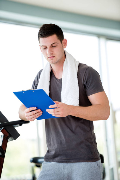 Portrait of a smiling male trainer with clipboard standing in a bright gym - Fotó, kép