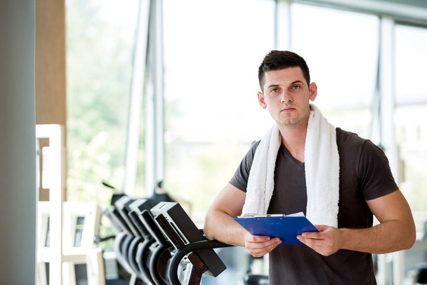 Portrait of a smiling male trainer with clipboard standing in a bright gym - Fotoğraf, Görsel