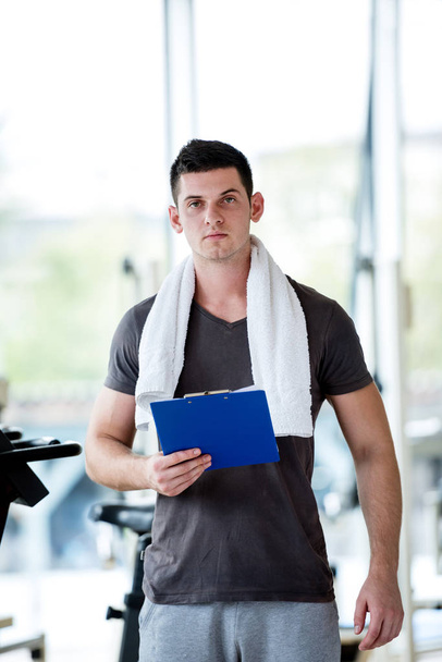 Portrait of a smiling male trainer with clipboard standing in a bright gym - Fotó, kép