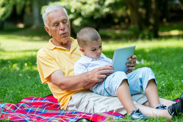 happy elderly senior grandfather and child in park using laptop computer - Photo, Image