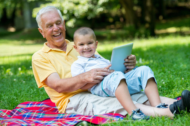 happy elderly senior grandfather and child in park using laptop computer - Foto, imagen