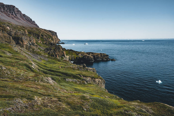 Arctic Beach avec petite cascade au Groenland. Près du petit village de Qeqertarsuaq, île Disko au Groenland. Ciel bleu avec océan et plantes vertes
. - Photo, image