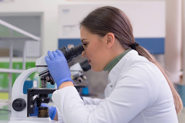 Mladá vědkyně se dívá pod mikroskop v laboratoři - Fotografie, Obrázek