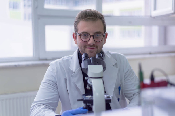 Joven científico masculino mirando a través de un microscopio en un laboratorio - Foto, Imagen