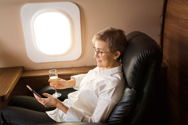 beautiful stylish woman aged, in the cabin of a private plane with a phone in her hand - Foto, immagini