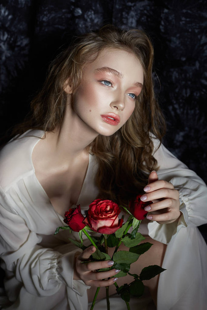 Beautiful spring girl is sitting on the floor with rose flowers  - Fotó, kép