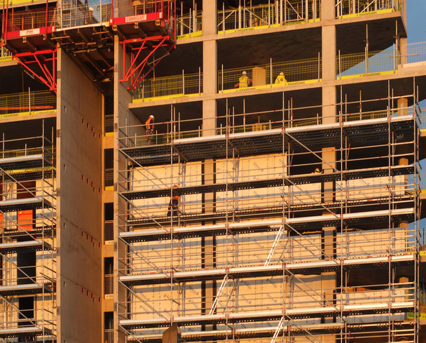 bouwers die werken op steigers en platformen op verschillende verdiepingen van een grote moderne bouwplaats - Foto, afbeelding