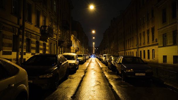 European street in light of yellow lanterns at night with cars in Parking. Concept. Straight beautiful street with residential buildings and parked cars lit by yellow lanterns at night - Zdjęcie, obraz
