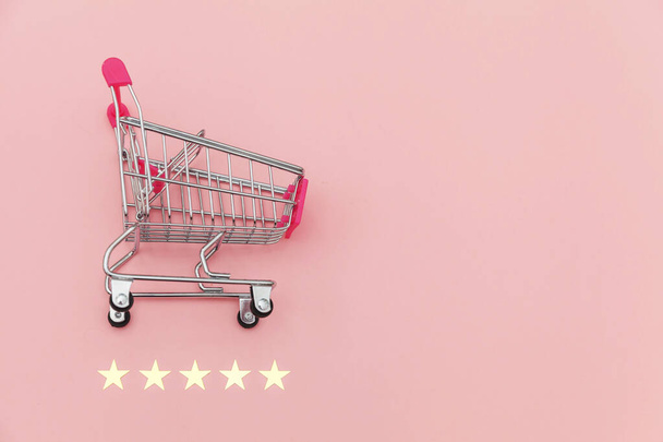 Pequeño supermercado carrito de compras empuje para juguete de compras con ruedas y clasificación de 5 estrellas aislado sobre fondo rosa pastel. Compras al por menor concepto de evaluación y revisión en línea
. - Foto, imagen