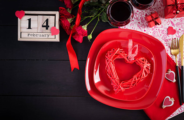 День святого Валентина ужин с сервировкой стола с подарком, красные розы, сердца с двумя бокалами вина на темном фоне. Вид сверху, плоский
. - Фото, изображение