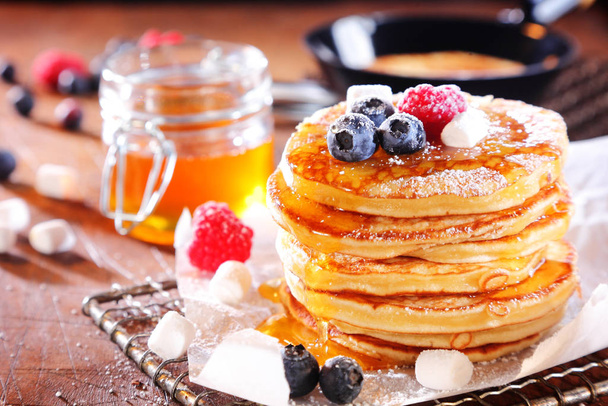 Stack of fresh golden pancakes or flapjacks topped with fresh autumn berries and drizzled with honey or syrup and white sugar - Foto, Bild