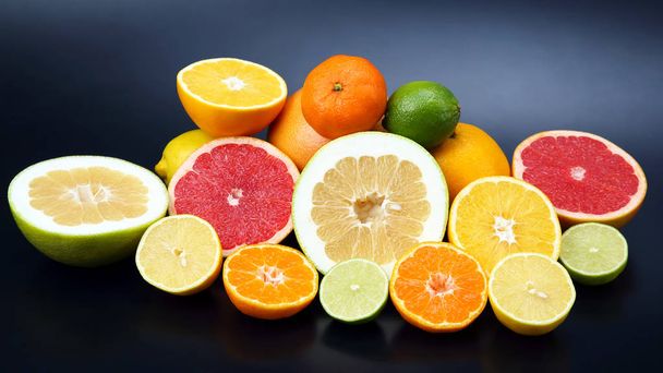 cut pieces of different citrus fruits on dark background - Photo, Image