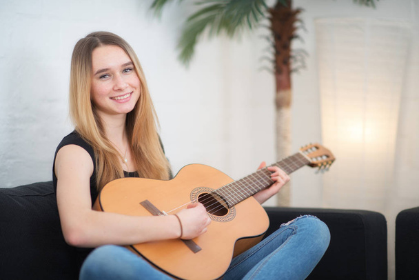 девушка сидит дома на диване и играет на гитаре - Фото, изображение