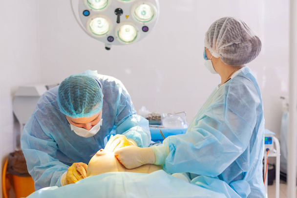 Hospital. Surgeon operates in the operating room. The surgeon places a suture on the breast after inserting the implant during breast augmentation surgery. - Foto, Imagem
