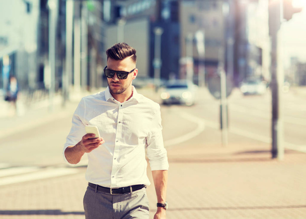 man in sunglasses with smartphone walking at city - Фото, изображение