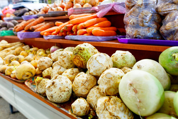 Сельдерей, репа, морковь, лук, корни и другие различные овощи продаются на полках рынка
. - Фото, изображение