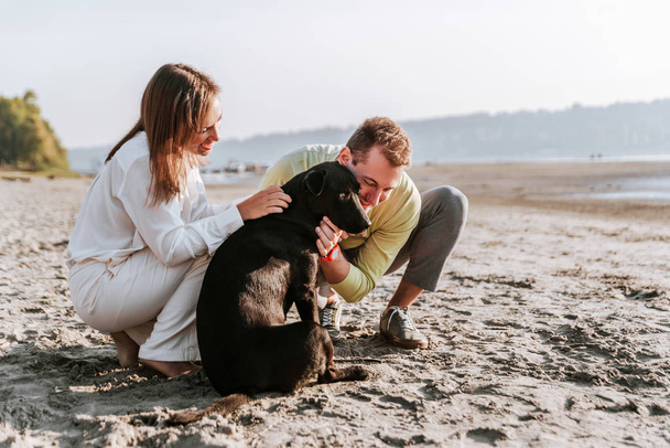 Ευτυχισμένο ζευγάρι περνούν τον ελεύθερο χρόνο τους στην παραλία με το σκυλί - Φωτογραφία, εικόνα