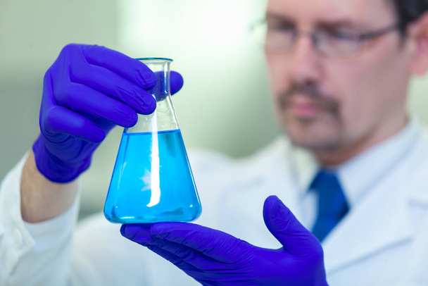 A scientist holds and studies a flask with blue liquid in a scientific laboratory - Fotó, kép