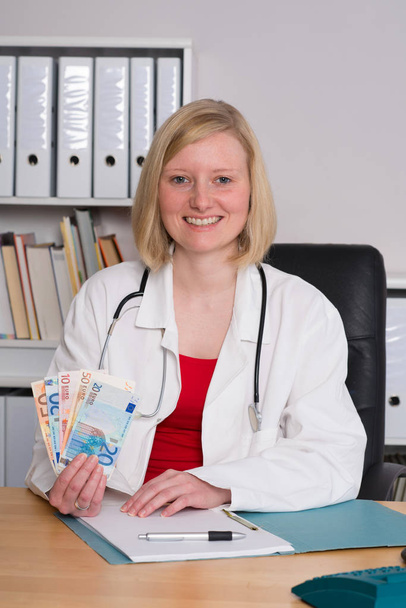young female family doctor in her office with money - Foto, imagen