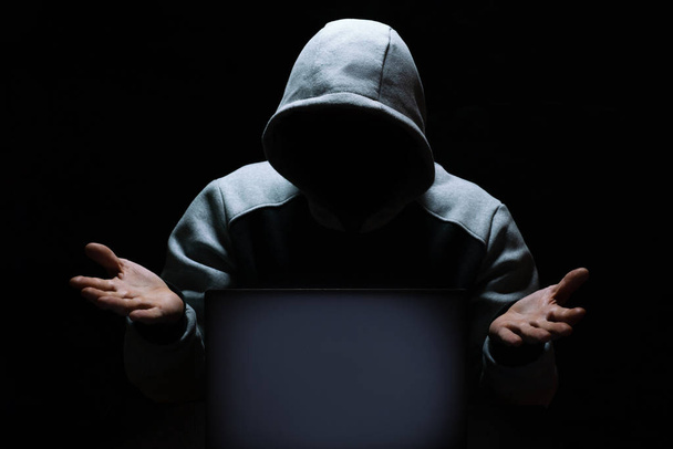 A computer hacker shrugs in disbelief in front of a laptop screen - Fotoğraf, Görsel