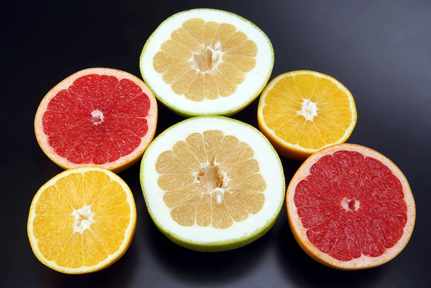 gesneden stukjes van verschillende citrusvruchten op donkere ondergrond - Foto, afbeelding